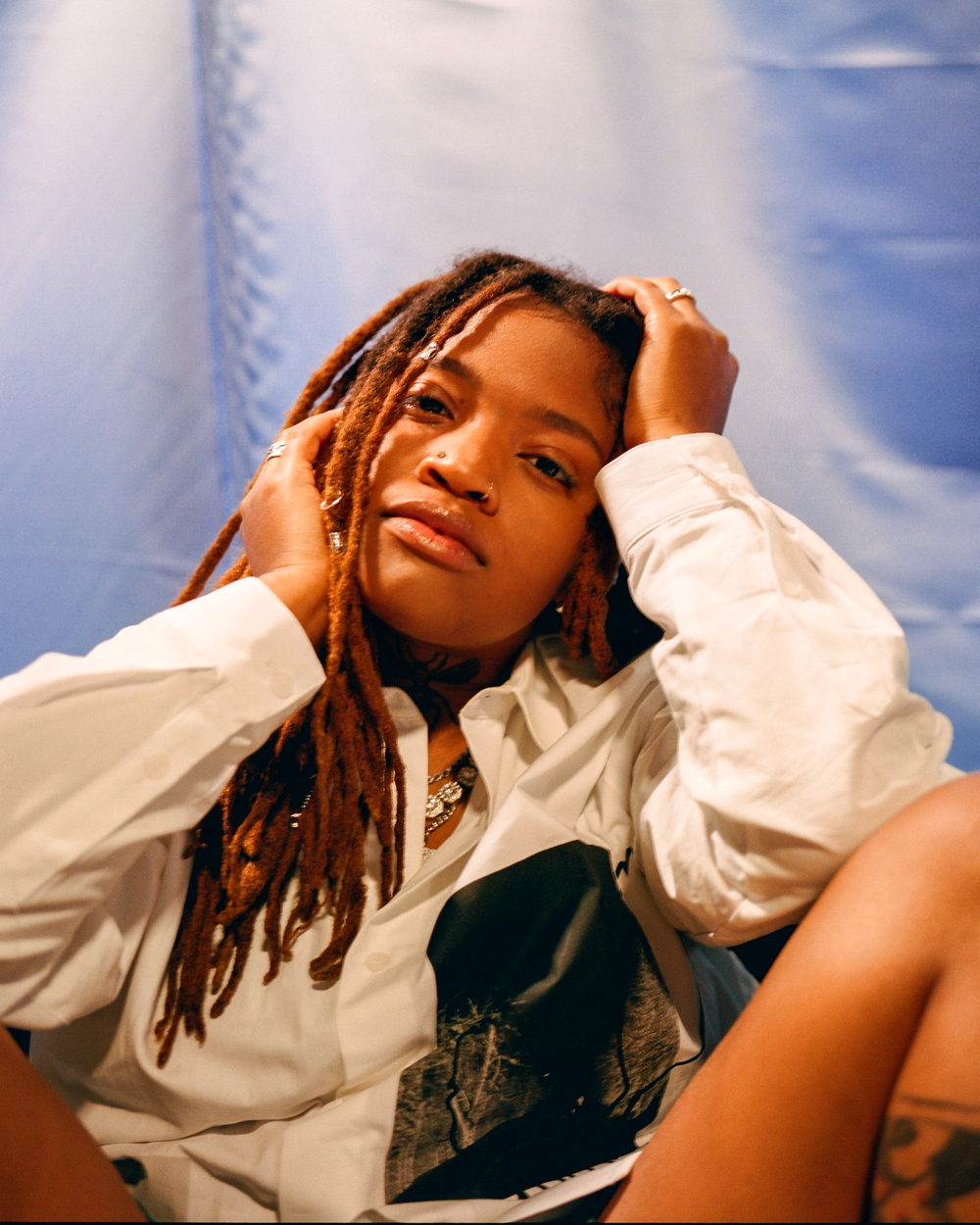 A woman with long locs resting against a pale backdrop