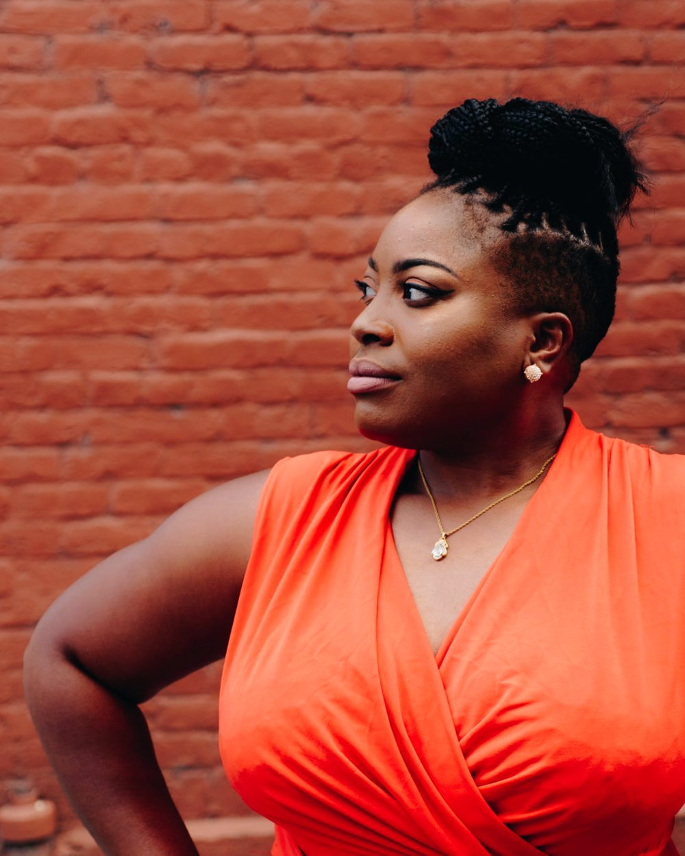 A woman with an updo standing against a brick wall