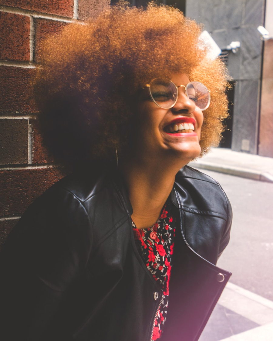A woman with a large curly afro laughing in the street