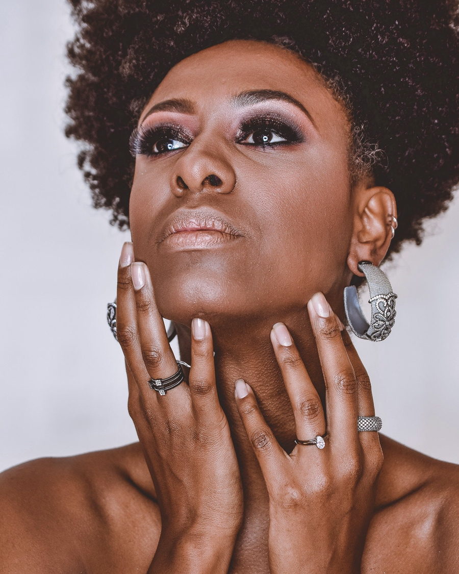 A portrait of a woman with a short natural cut, hands raised