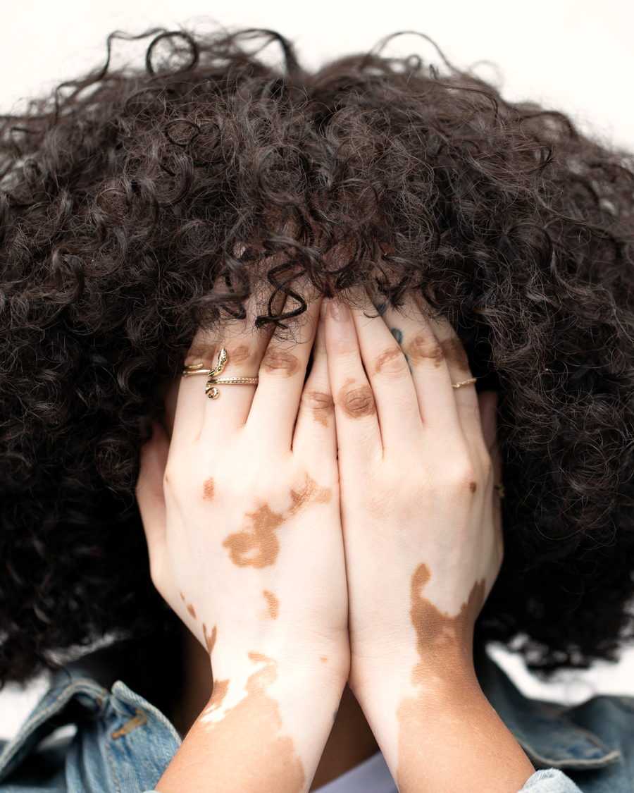 A woman with a large curly afro resting her hands over her face